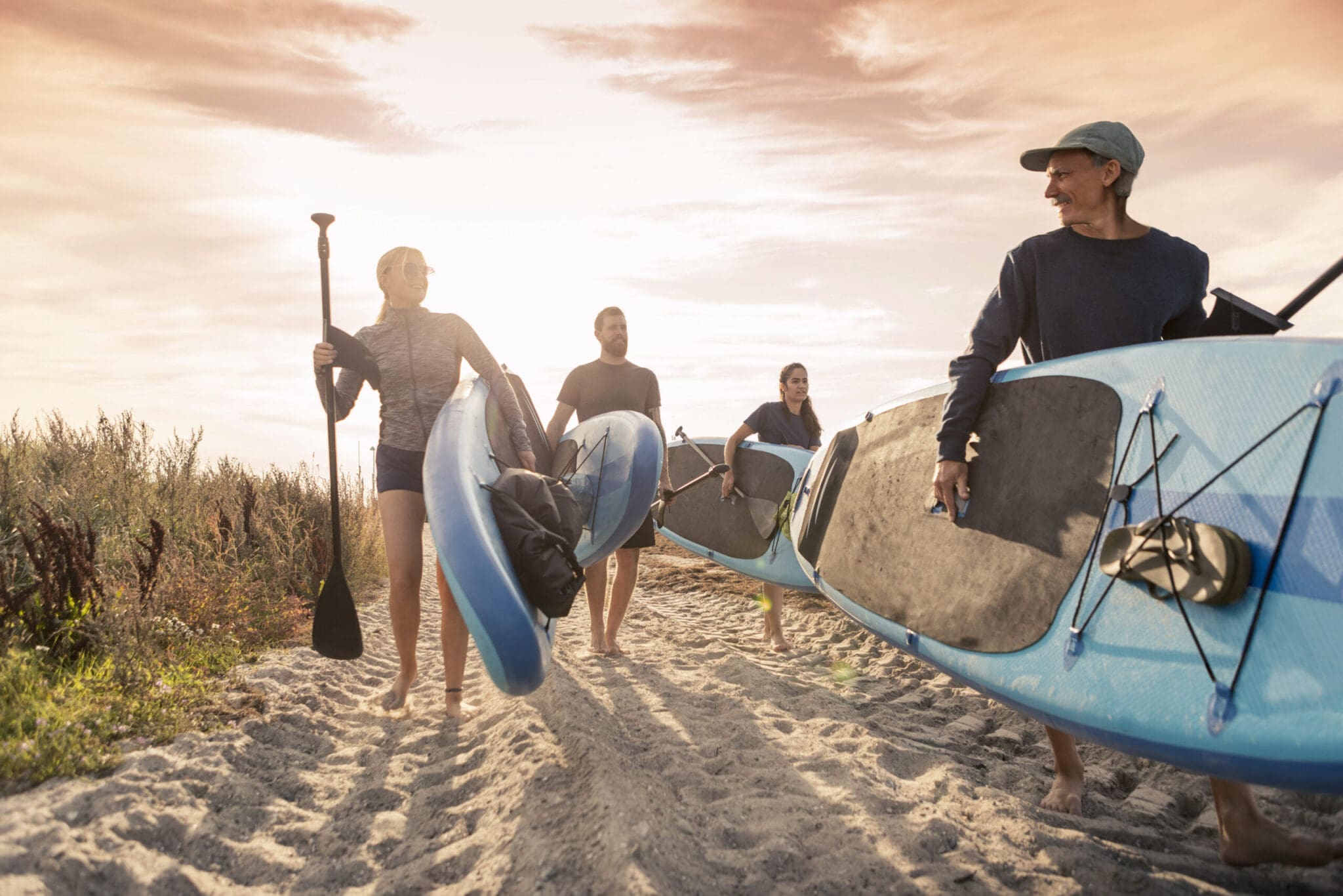 Male and female friends carrying paddleboard at sandy beach during sunset